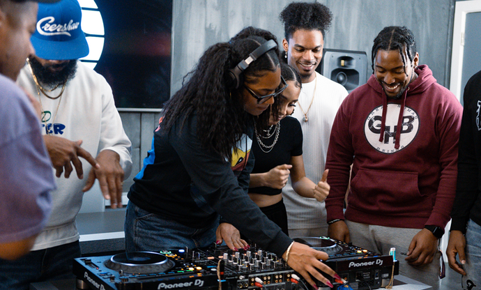 woman using turntables with headphones and 3 people watching her